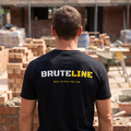 Bricklayer on site wearing the black BruteLine t-shirt, showing the BRUTELINE print and BUILT TO HOLD THE LINE across the back
